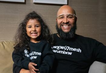A young smiling girl sits with a smiling bearded man who has his arm around waste.