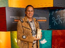 A man wearing a buckskin jacket stands in front of a wall of blocks of colours. He holds an award.