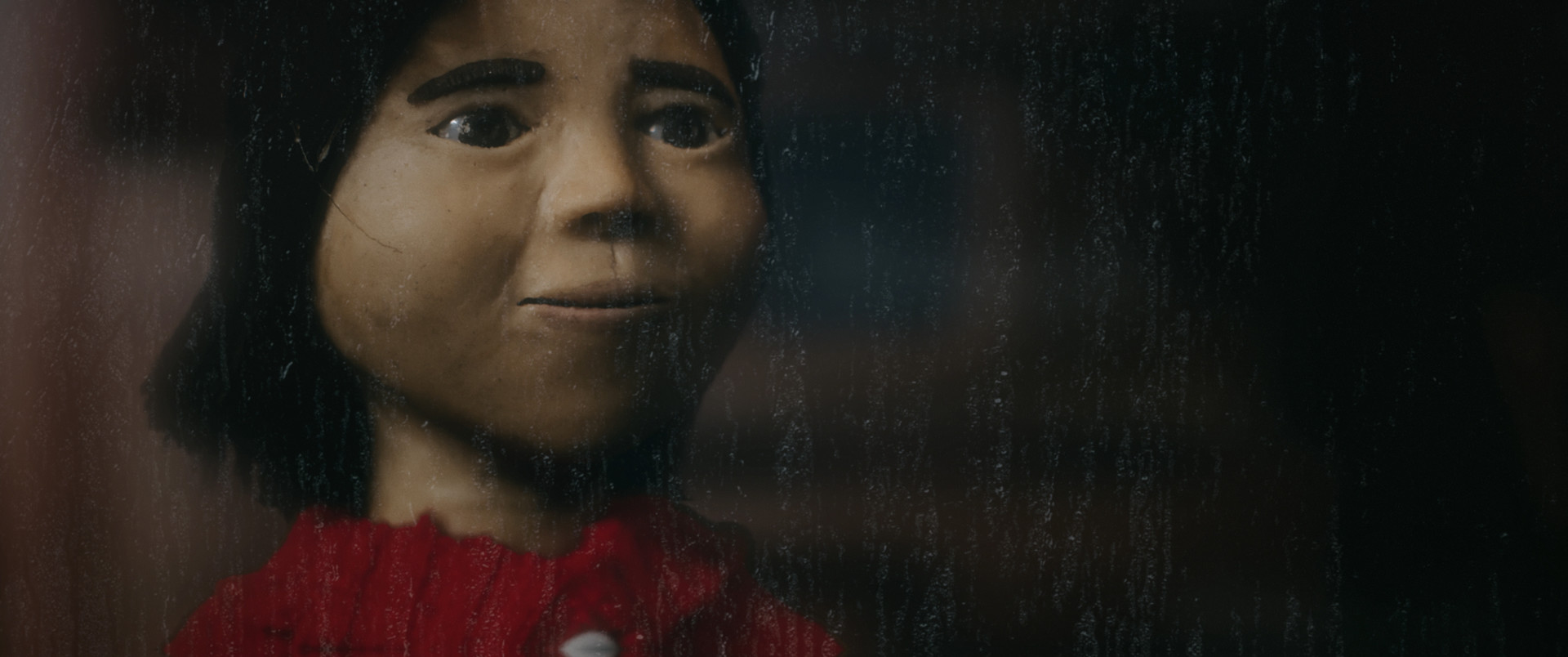 Claymation figure of a young girl with short dark black hair. She is wearing a red sweater.