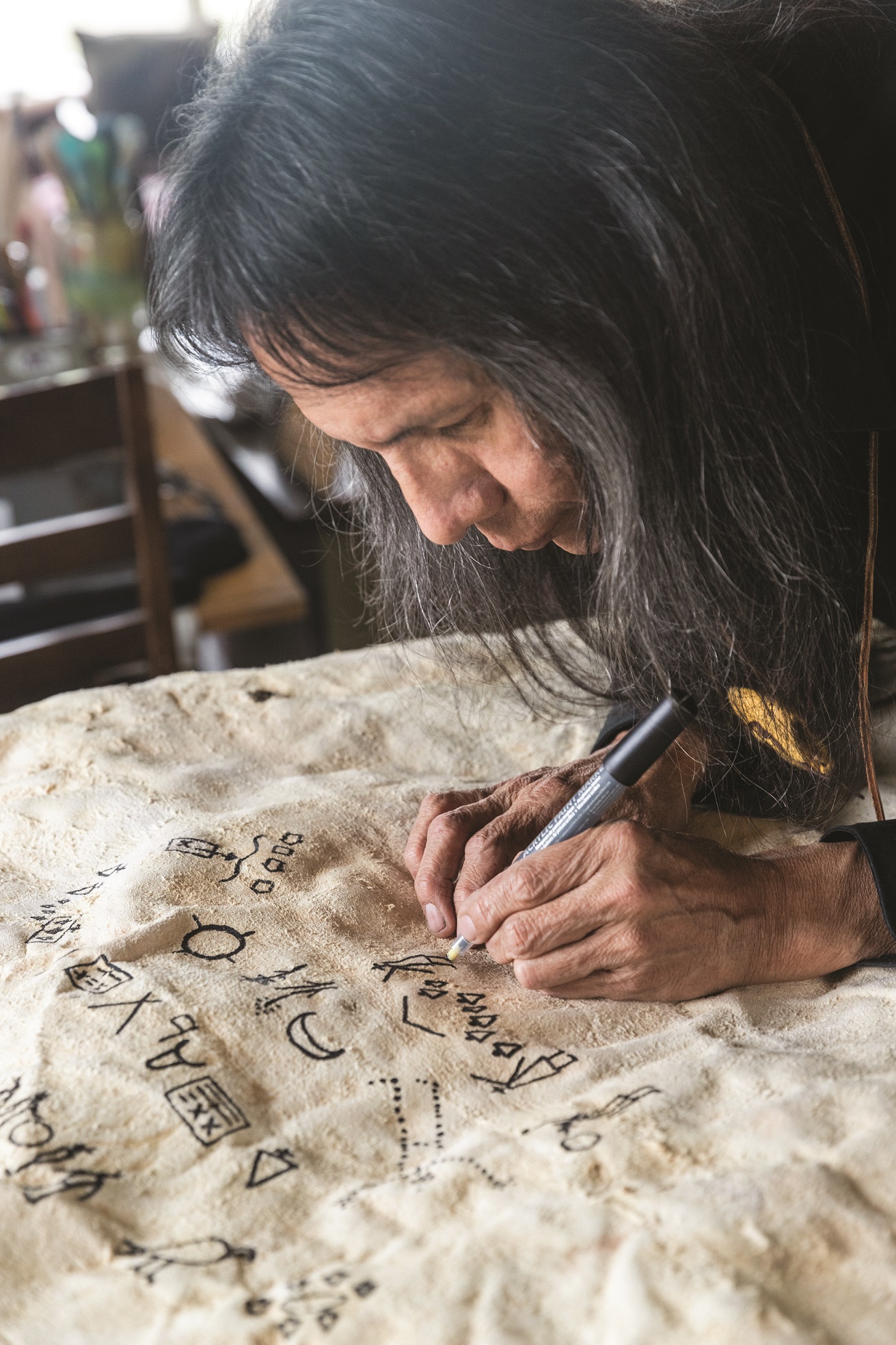 A man is bent over to draw symbols in black on a buffalo robe.