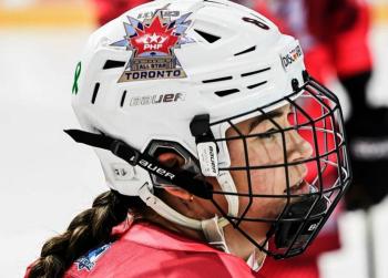 A woman wearing a white helmet with an PHF All-Star logo on it has a braid flowing down the back of her red jersey.