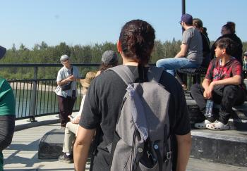 A grey-haired woman speaks to a group of people on a bridge. 