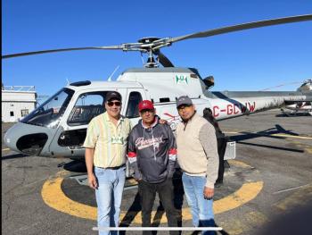Three men stand in front of a helicopter.