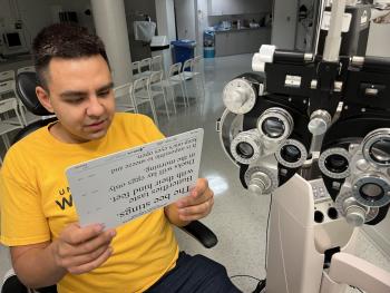 A man sits in an optometry office. He holds a vision test card in front of him.