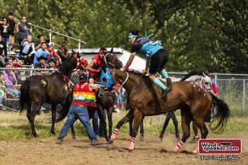 A rider jumps onto a horse to ride bareback around the track. People around him hold back other horses to clear the rider's way.