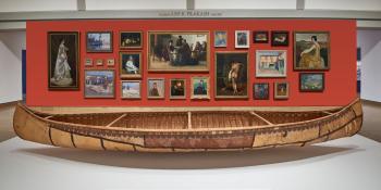 A birchbark canoe is dispayed before a wall of painting.