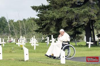 Pope Francis sits in his wheelchair amongst white wooden crosses in a cemetary and prays.