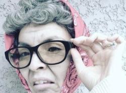 Comedian Joyce Delaronde is made up as an old lady wearing a pink head scarf