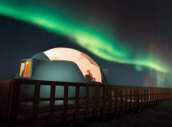 A dome shines against a dark sky lit up by northern lights.