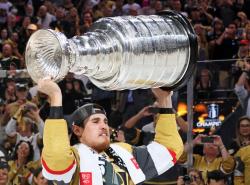 A beard man in a hockey uniform raises the Stanley Cup above his head.