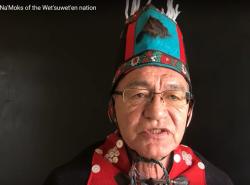 A coastal First Nations chief in traditional regalia, including button blanket.