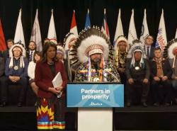 A woman and a man stand at a podium. The man wears a chief's feather 